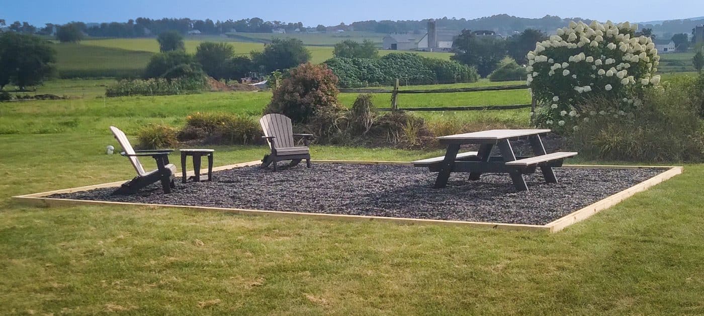 A gravel patio area for a fire pit with chairs and a picnic table
