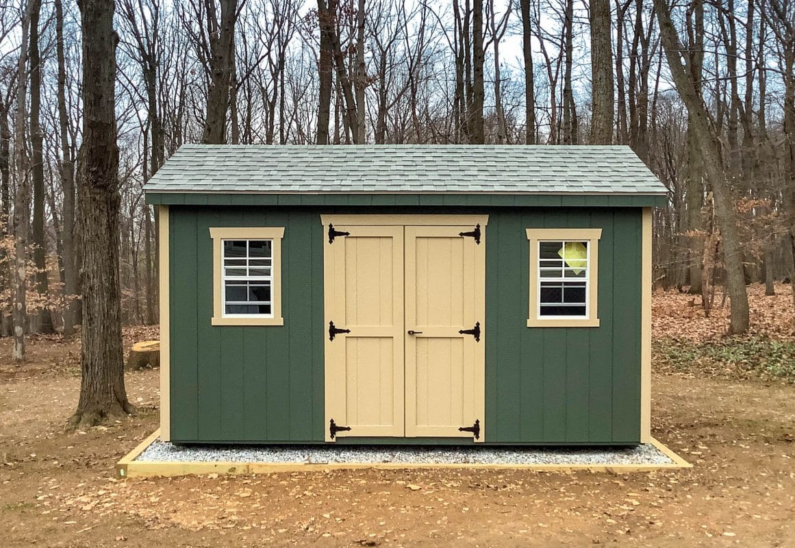 A green shed that is anchored into gravel.