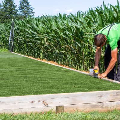 worker fastening turf to perimeter in artificial grass installation process