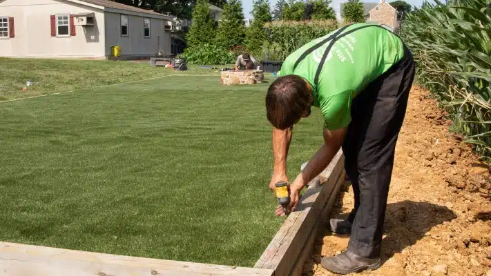 worker securing turf to wooden perimeter for turf installation process
